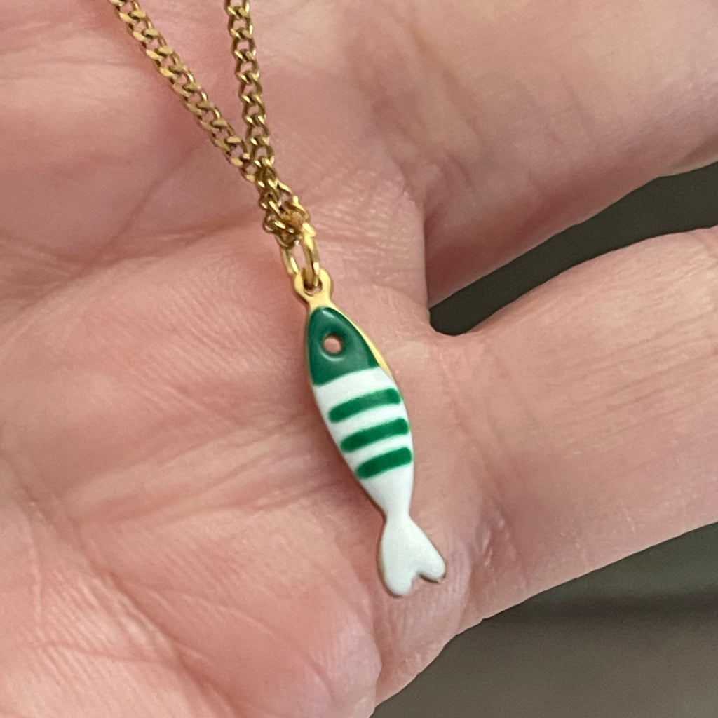 Green and white striped fish pendant on a gold chain held in a hand.