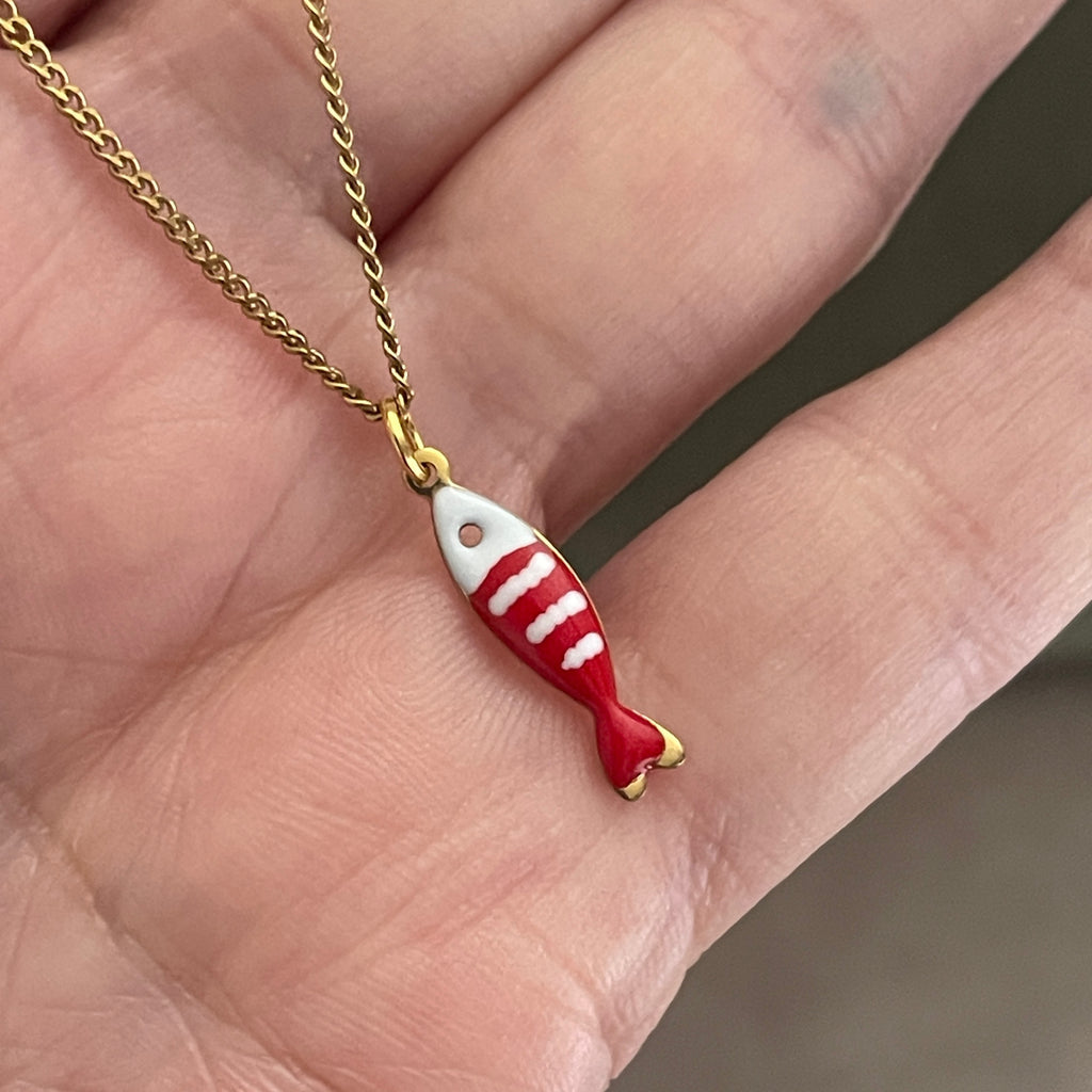 Red and white fish-shaped pendant on a gold chain held between fingers.