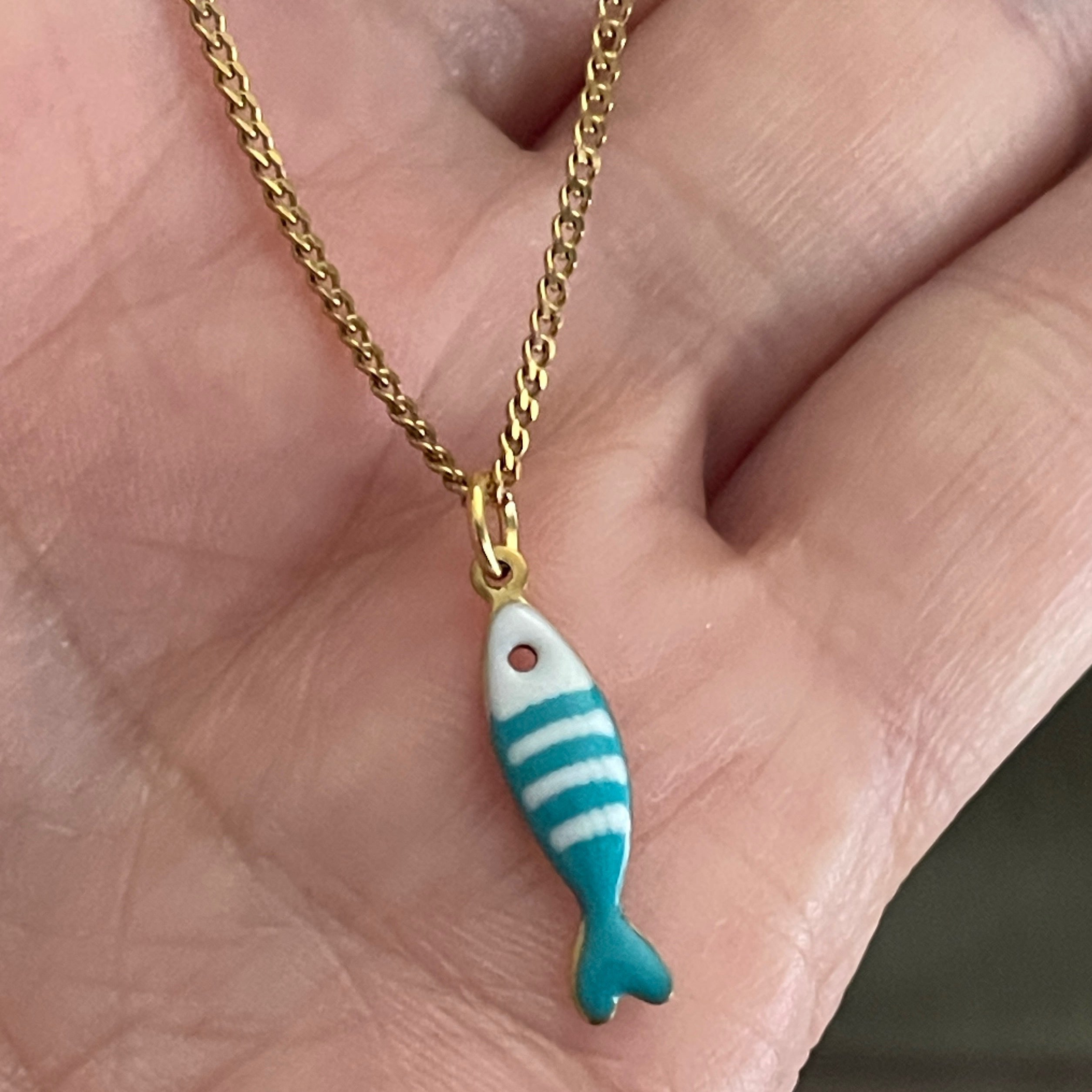 Gold chain with a blue and white striped fish pendant held in a hand.