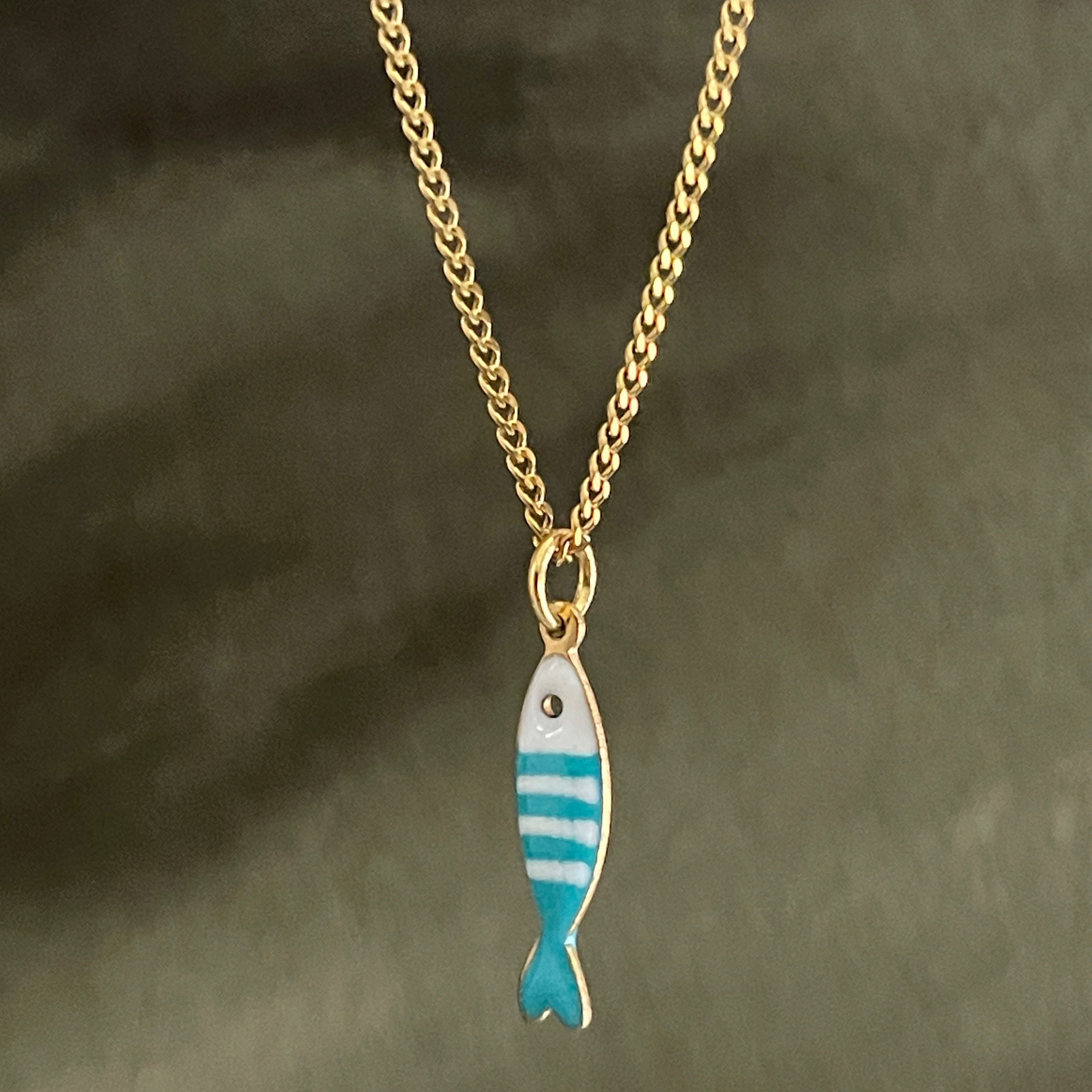 Gold chain necklace with a turquoise and white fish pendant on a dark background
