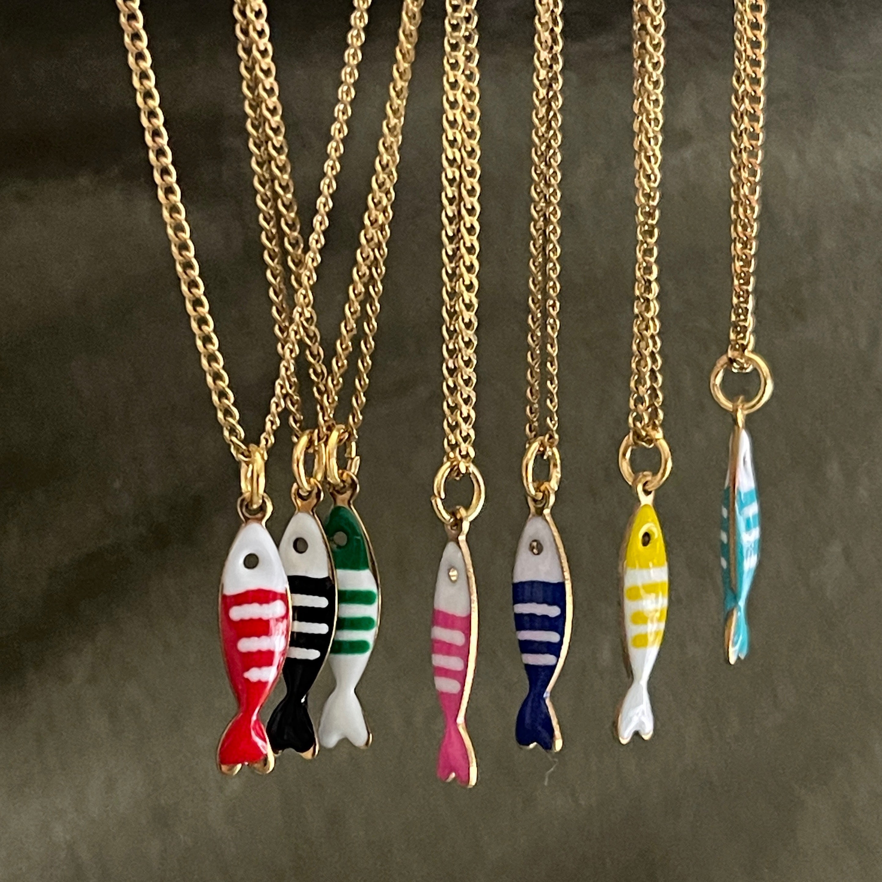 Gold necklaces with colorful fish pendants on a dark background