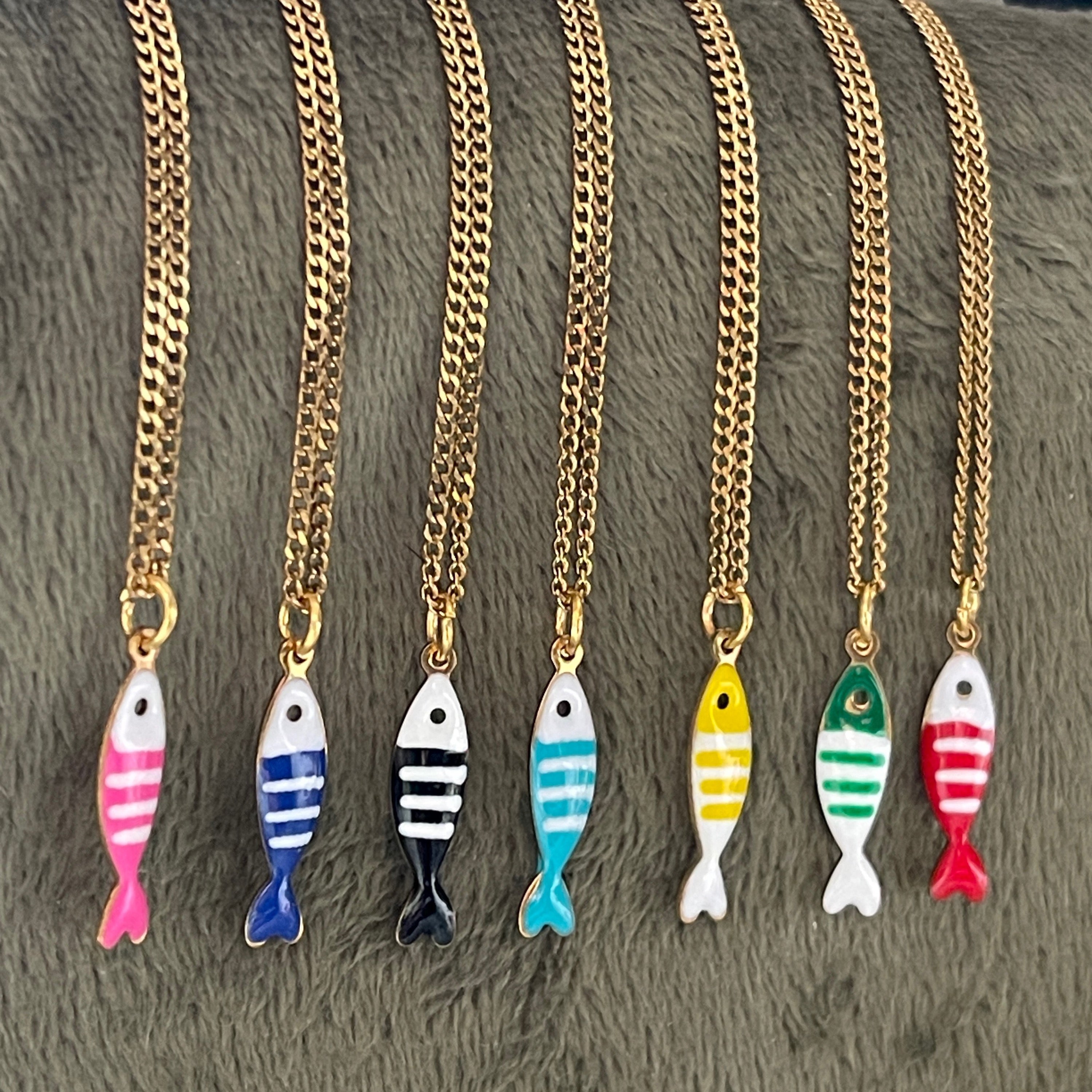 Gold chain necklaces with colorful fish pendants on a textured surface