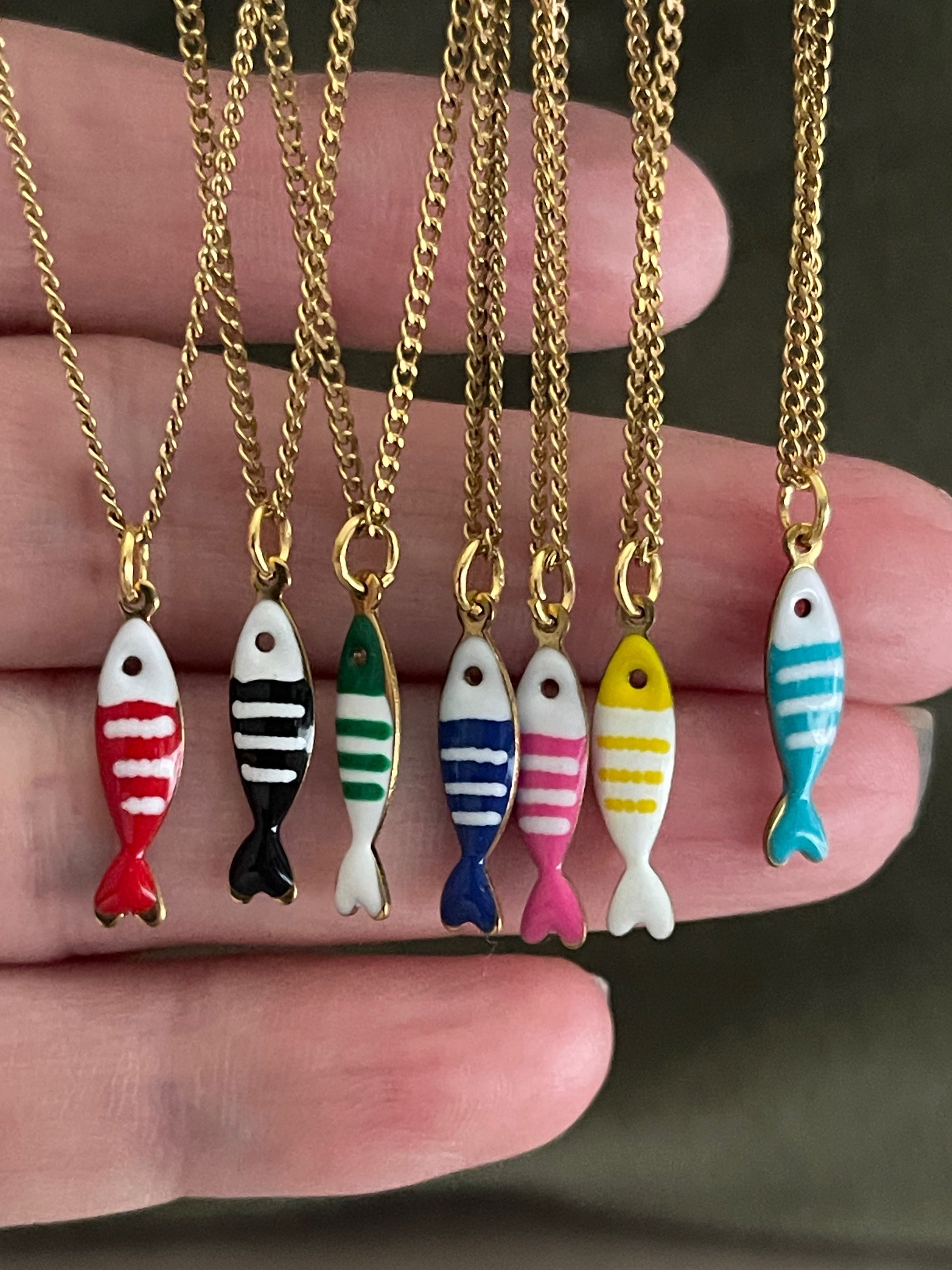 Colorful fish-shaped pendants on gold chains held by a hand.
