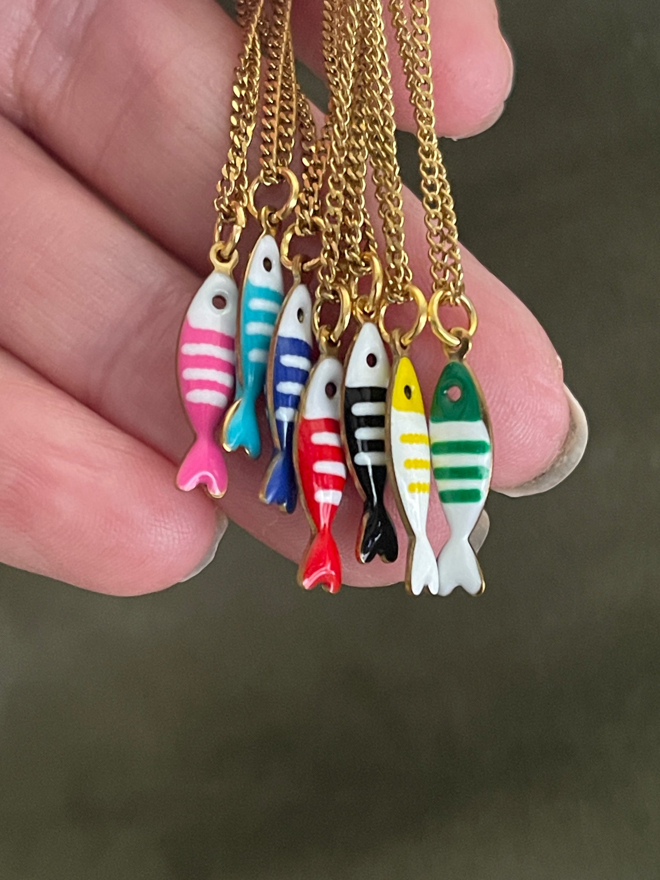 Colourful fish-shaped pendants on gold chains held by a hand against a dark background