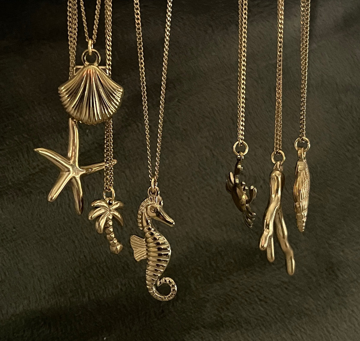Gold necklaces with various sea-themed pendants on a dark background