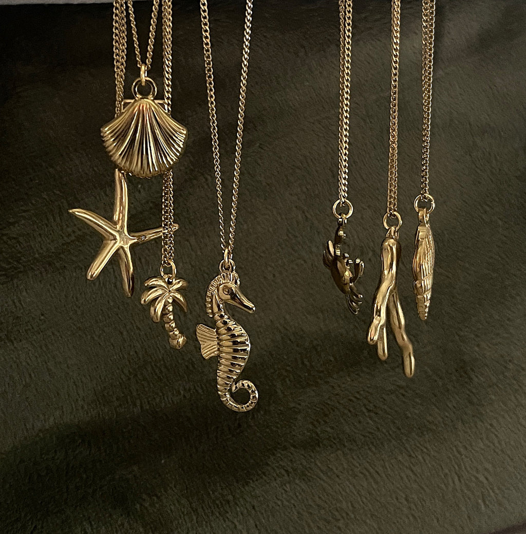 Gold necklaces with various sea-themed pendants on a dark surface