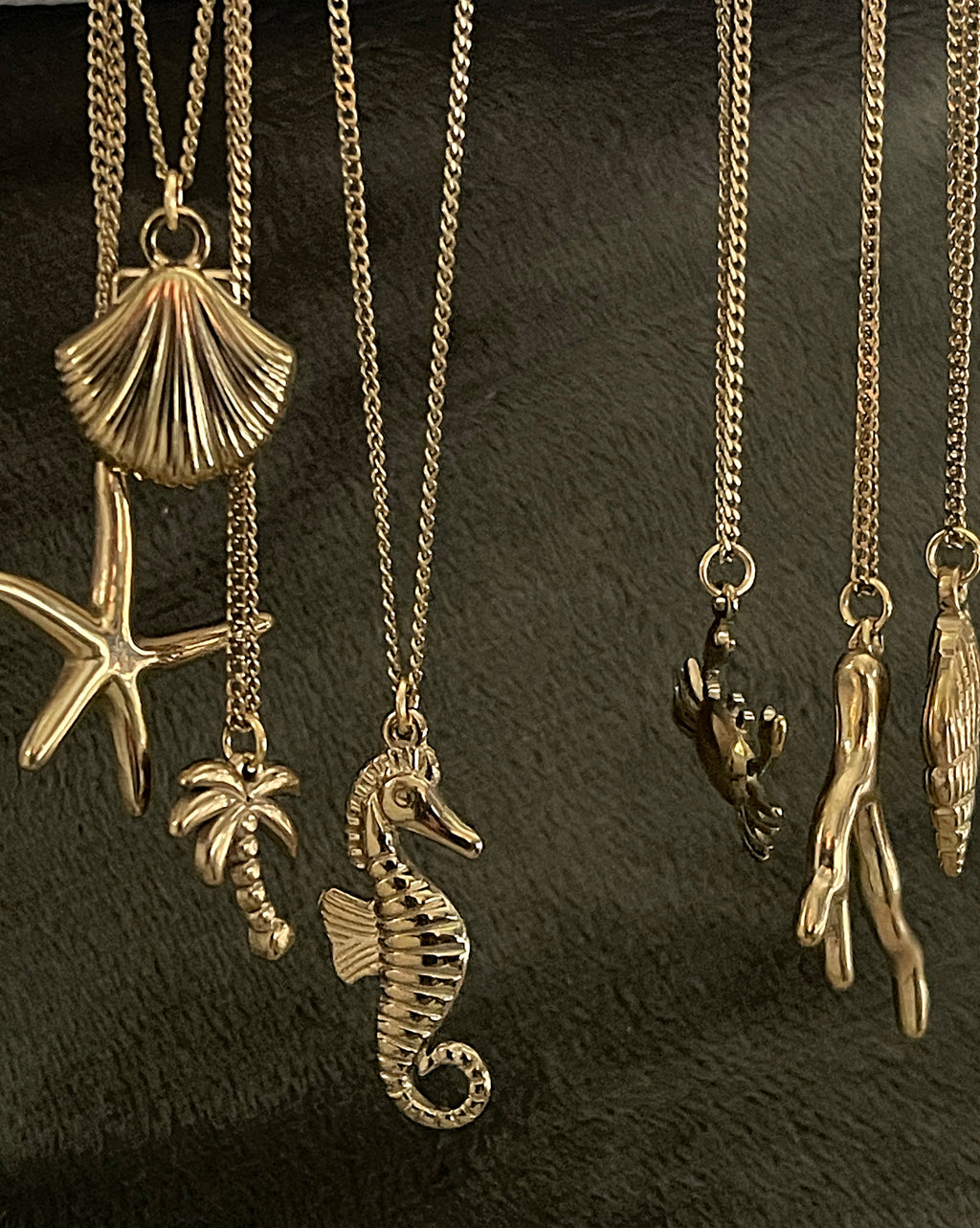 Collection of gold necklaces with various pendants on a dark background