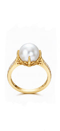 A yellow gold ring featuring a large, round white pearl in a prong setting, with small clear stones along the shoulders, shown against a plain white background.