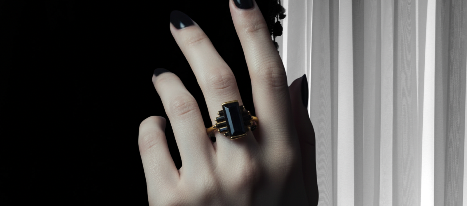 A hand with black nails wearing a black and gold ring against a black and with textured background. 