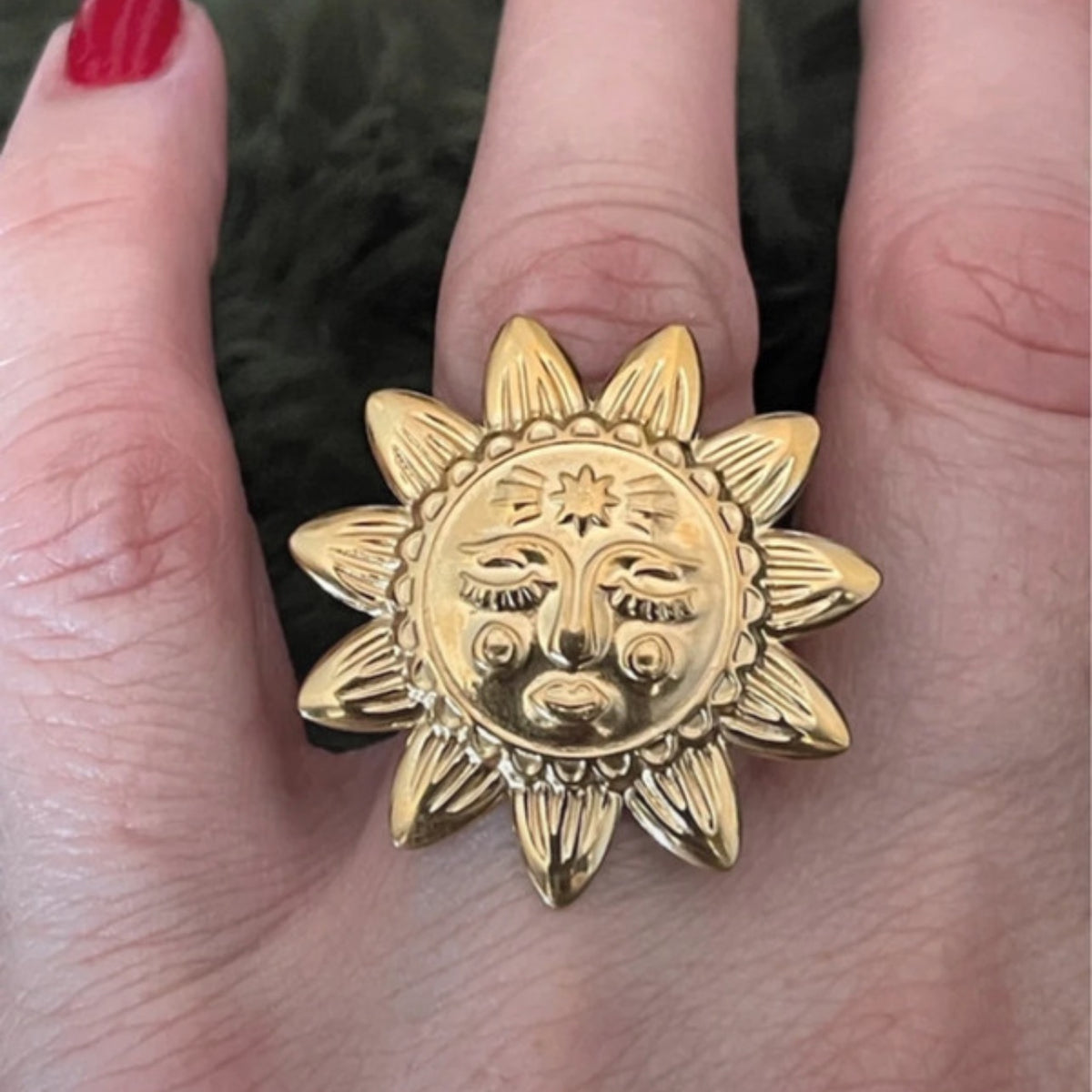 Gold sun-shaped ring with face design held between fingers