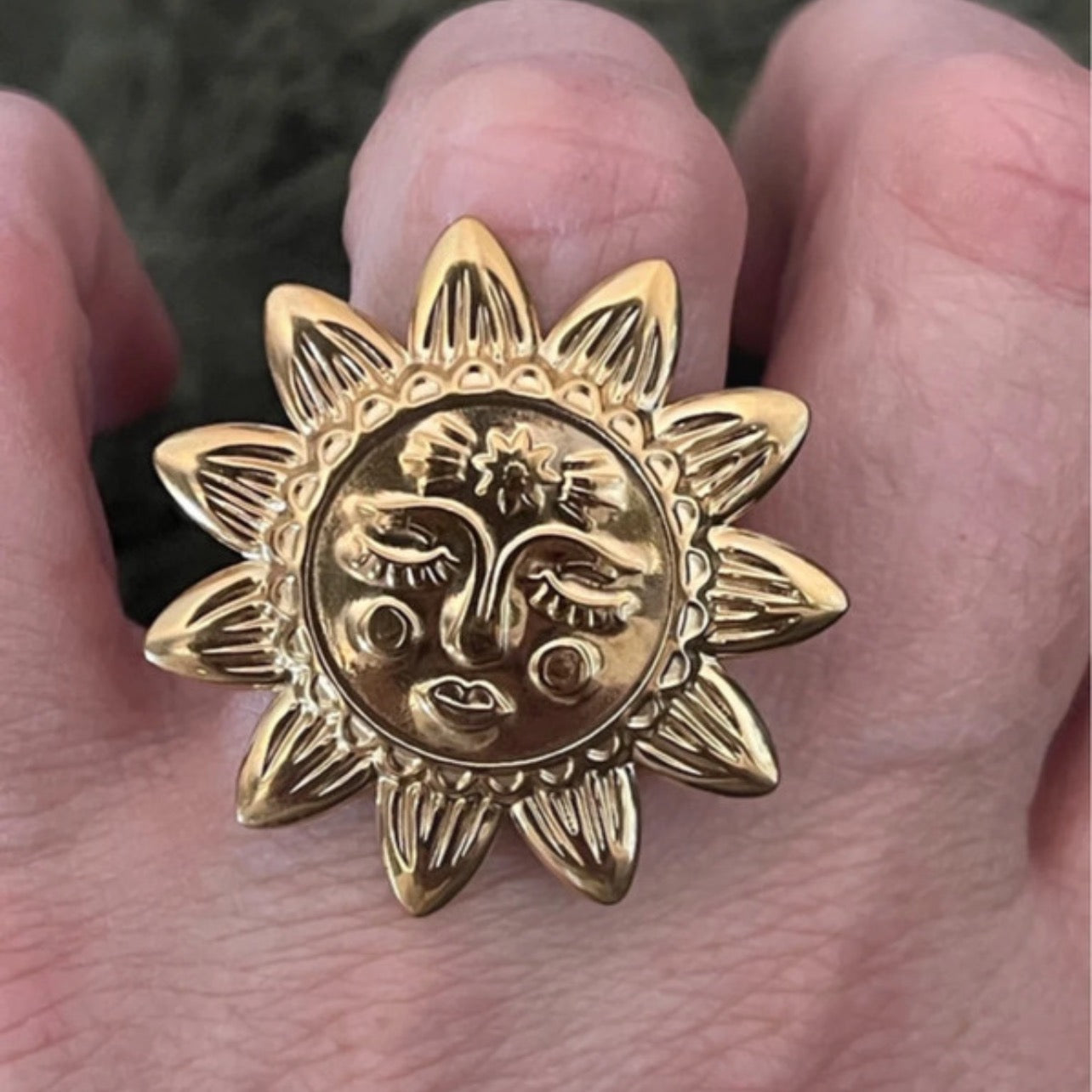 Gold sun-shaped ring with face design held in a hand.