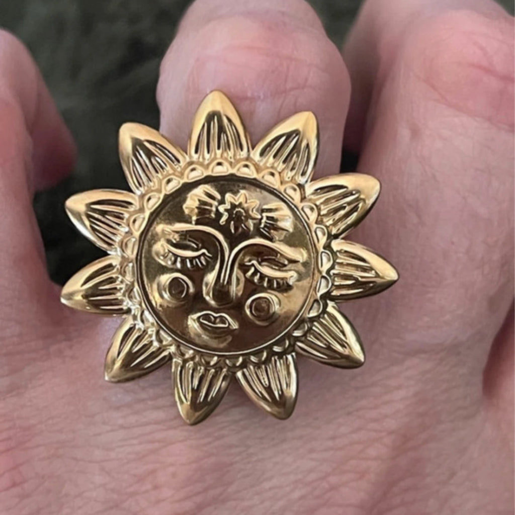 Gold sun-shaped ring with face design held in a hand