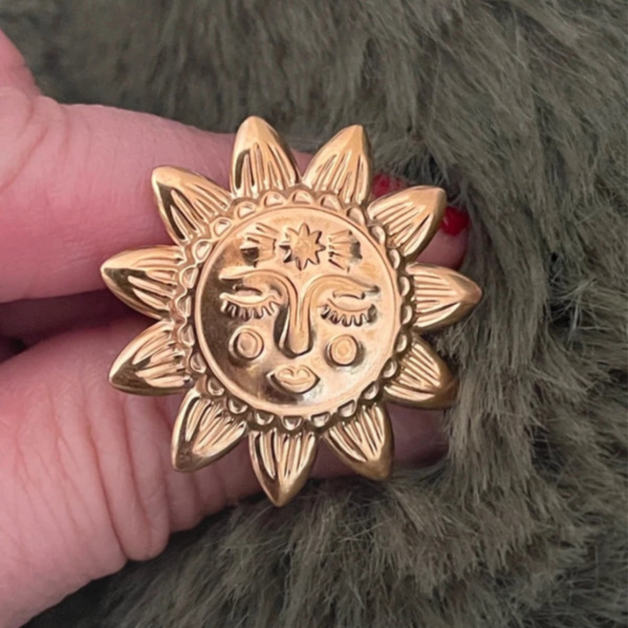 Gold sun-shaped ring held by a hand against a textured green background