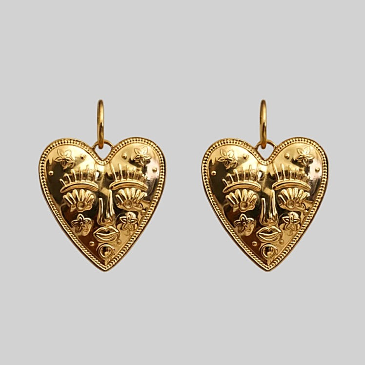 Gold heart-shaped earrings with intricate designs on a light gray background