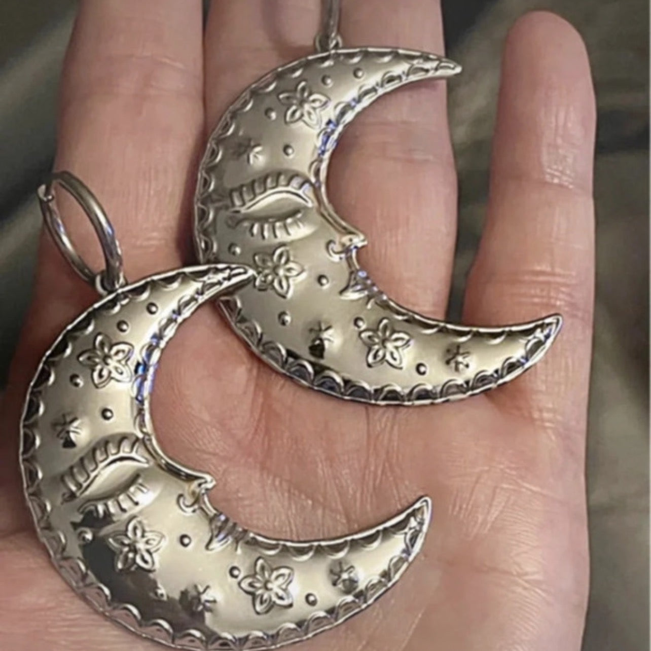 Silver crescent moon earrings held in a hand