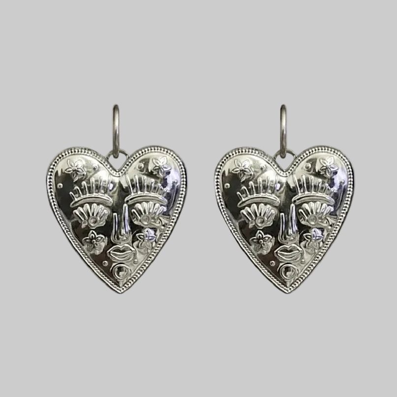 Pair of silver heart-shaped earrings with intricate designs on a light gray background