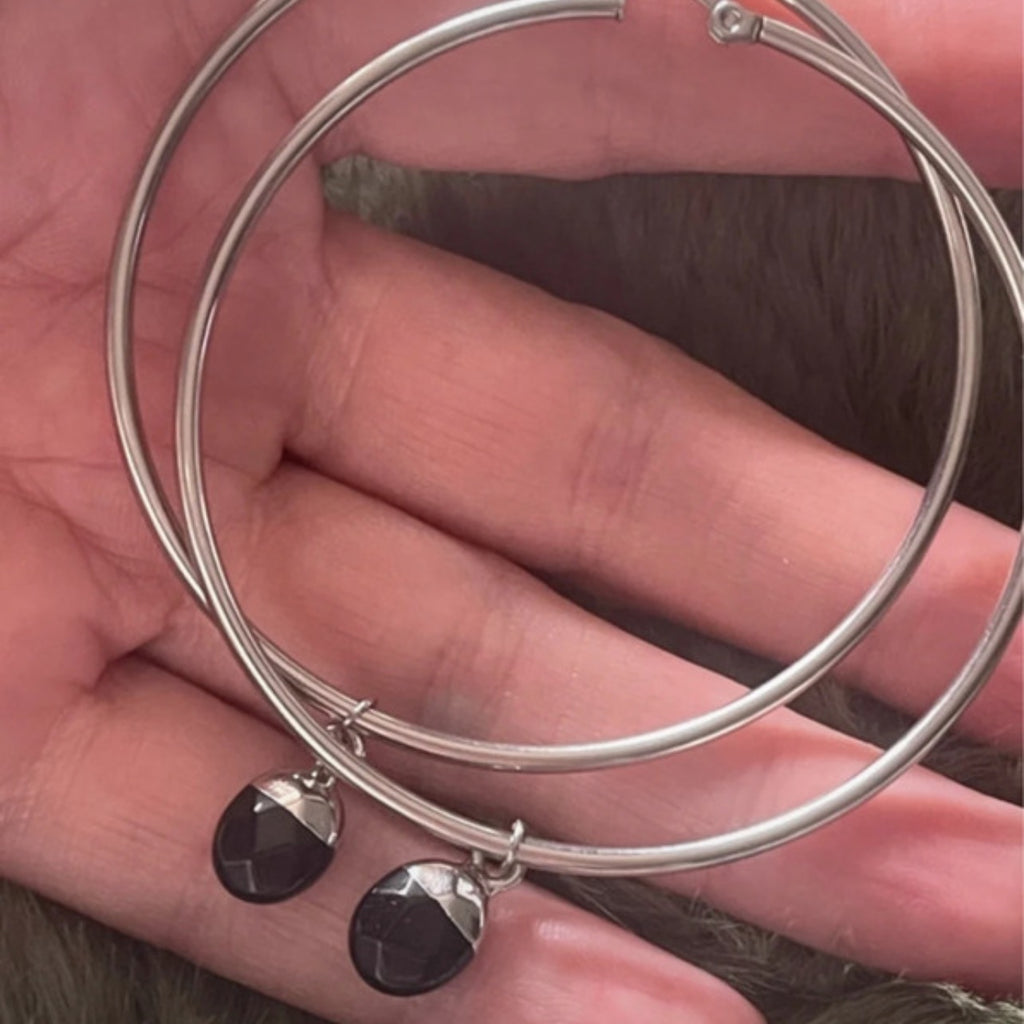 Silver hoop earrings with black crystals held in a hand