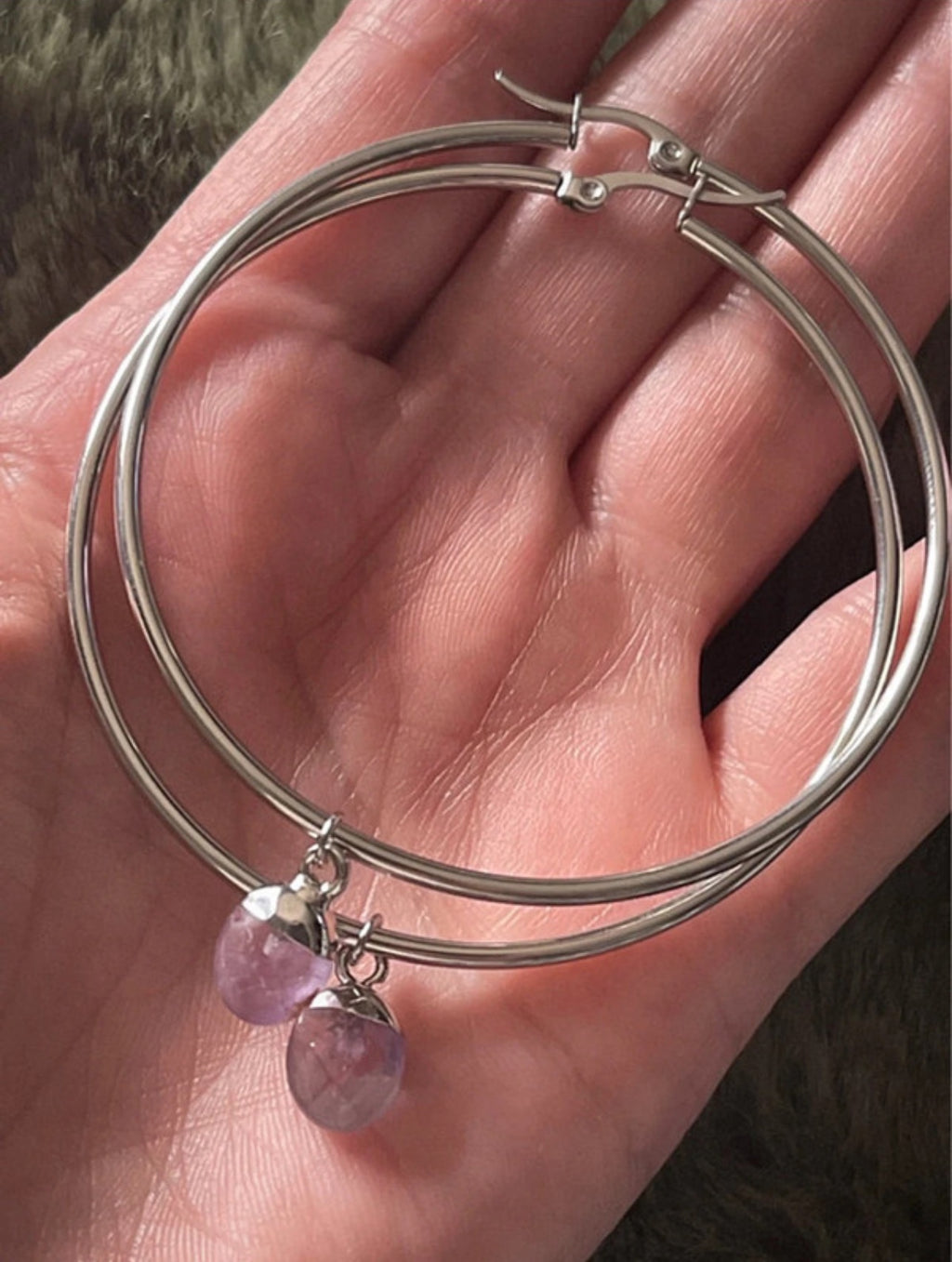 Silver hoop earrings with purple crystals on a hand