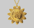 A gold pendant necklace featuring a stylized sun face surrounded by rays, suspended from a gold chain against a solid gray background.