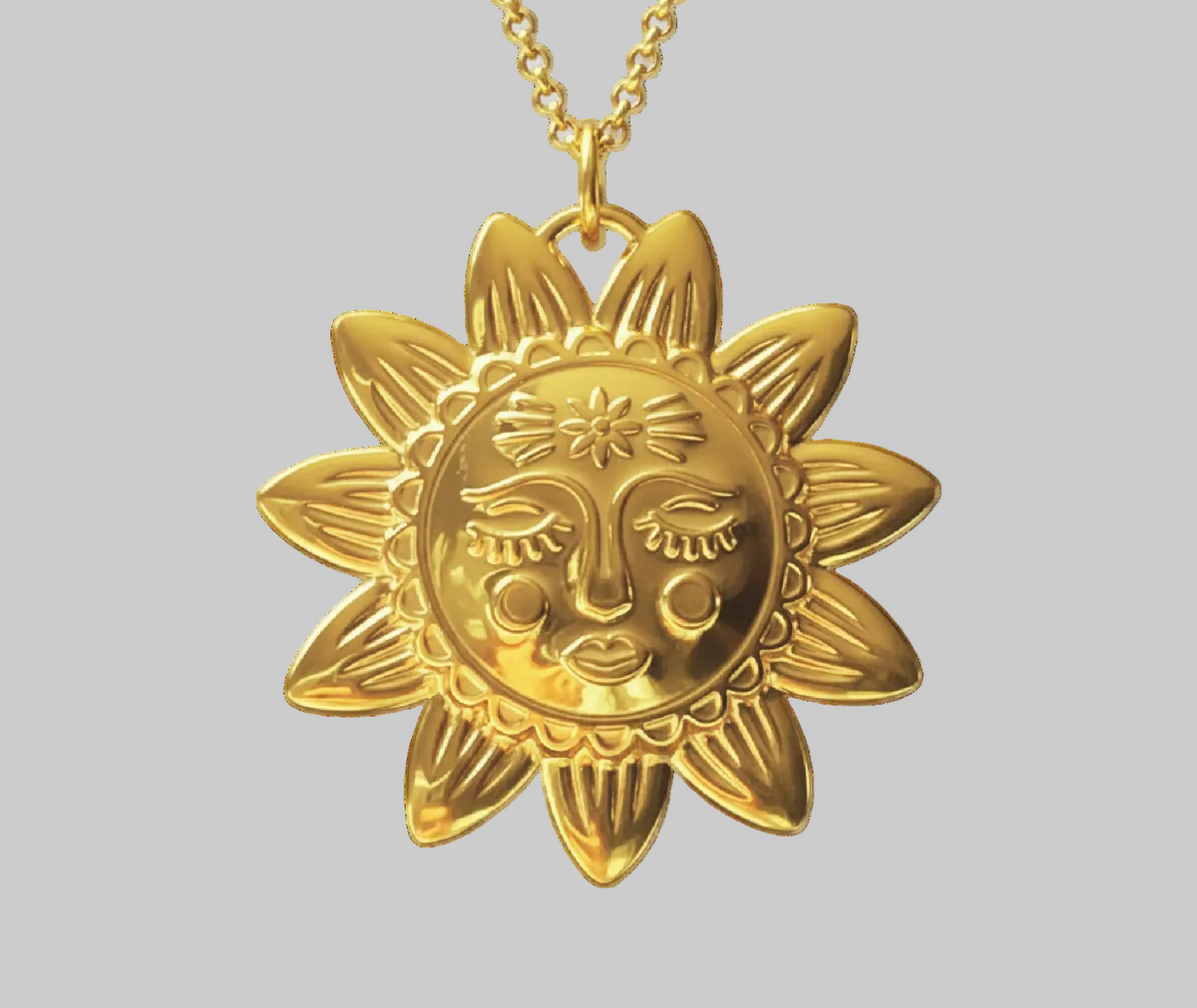 A gold pendant necklace featuring a stylized sun face surrounded by rays, suspended from a gold chain against a solid gray background.