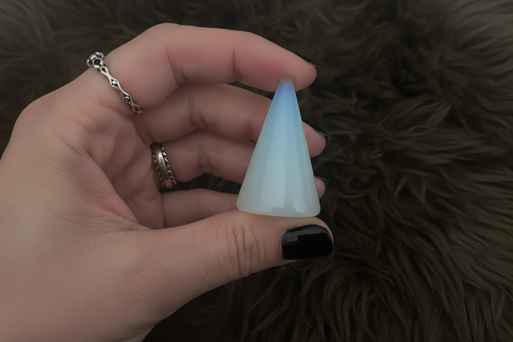 Hand holding a cone-shaped opalite crystal against a dark, textured background