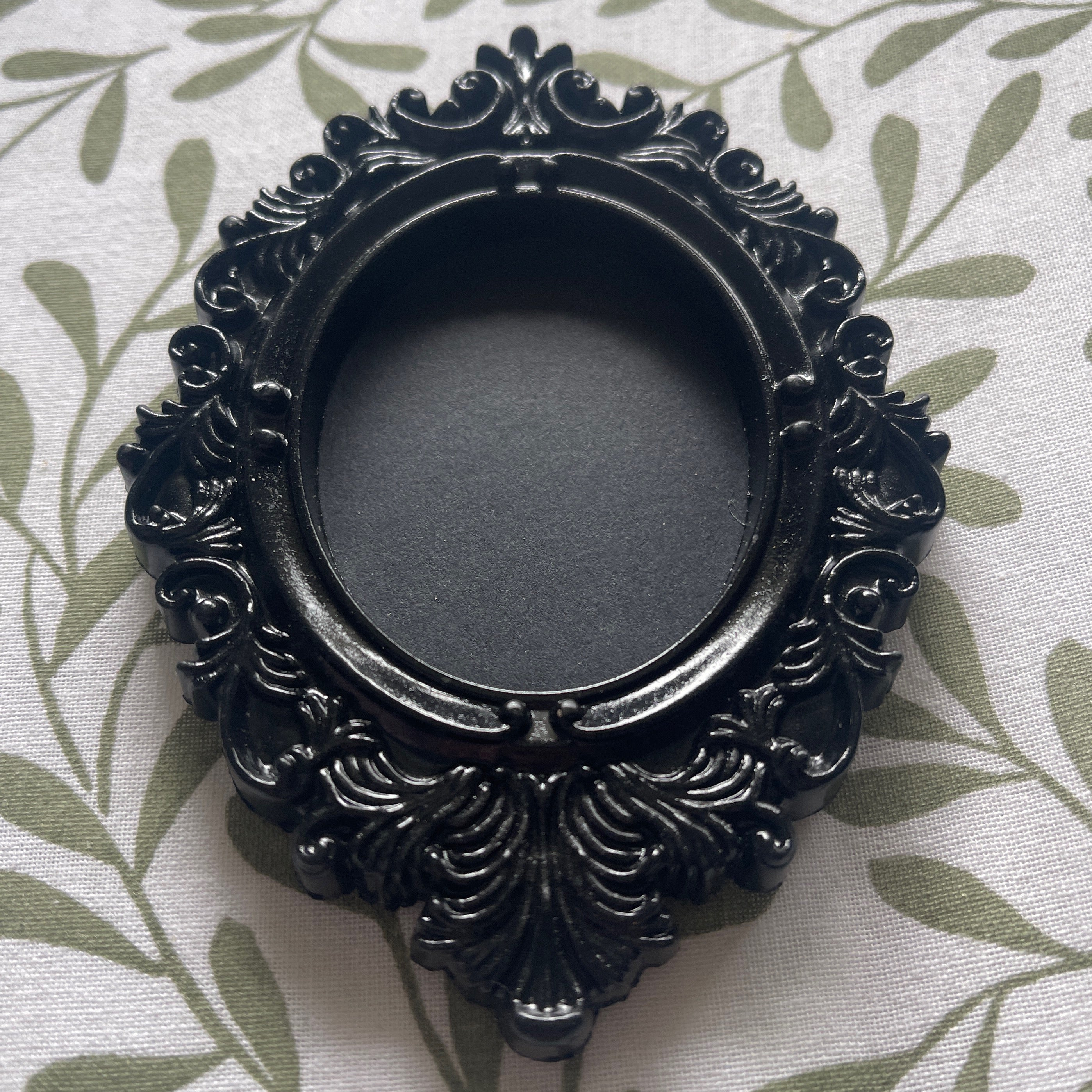 Decorative black circular object with intricate patterns on a leaf-patterned fabric background