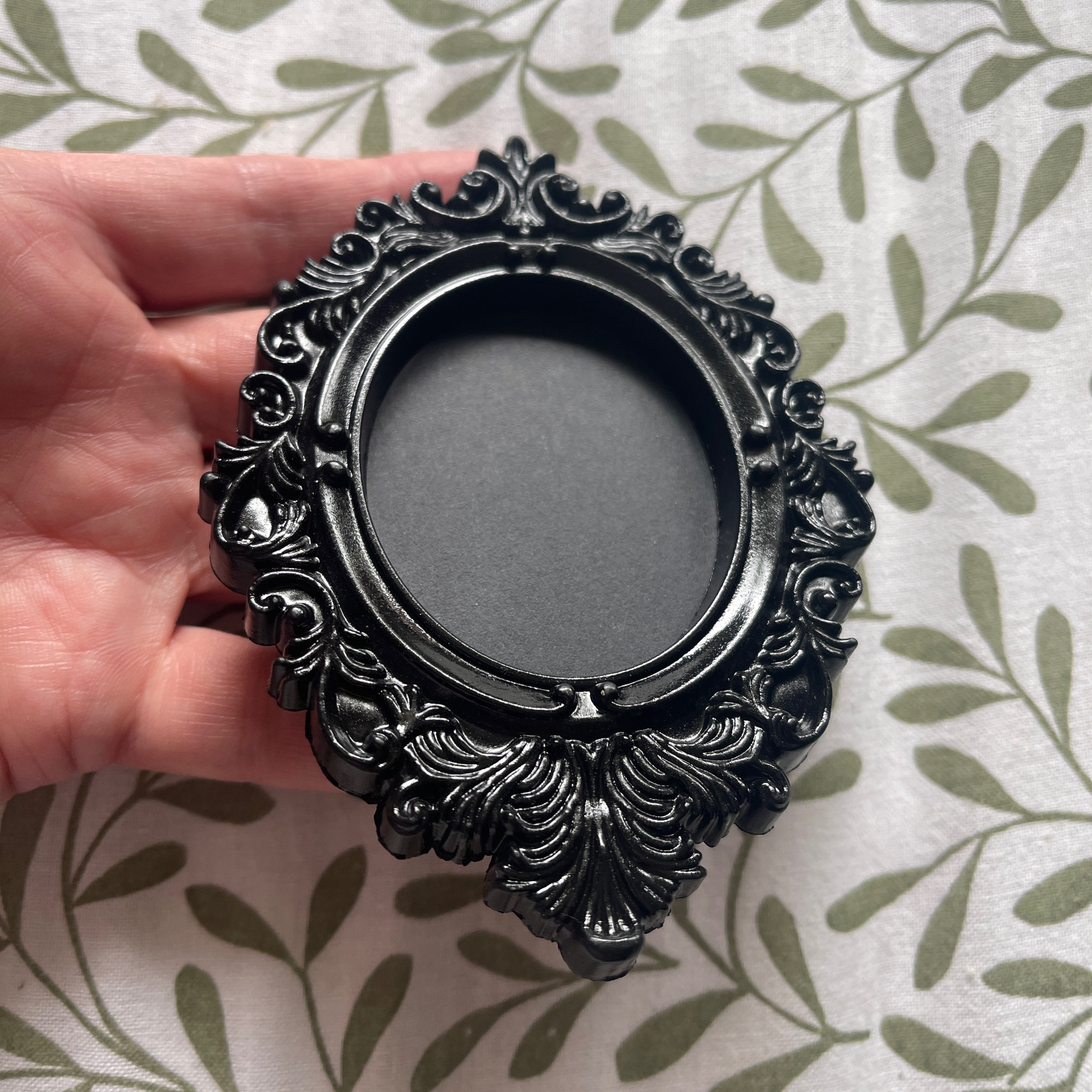 Decorative black frame held by a hand on a patterned background