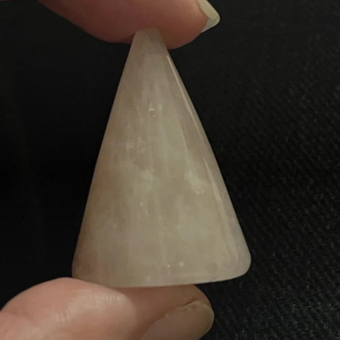 Triangular stone held between fingers against a dark background