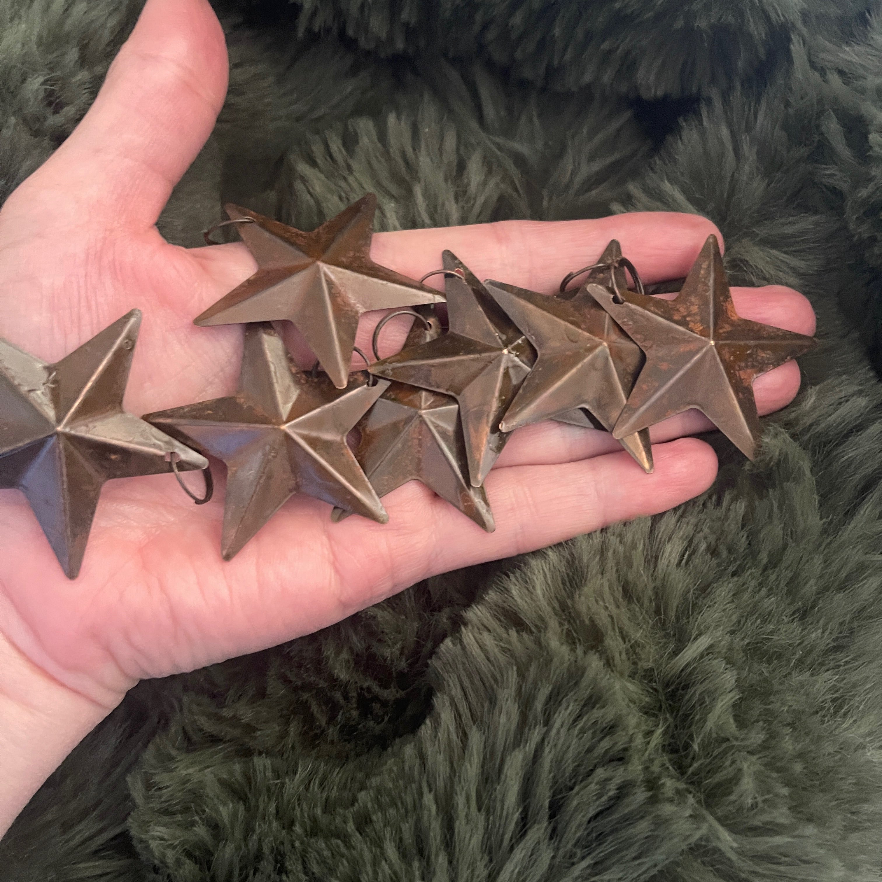 Hand holding bronze star-shaped ornaments against a green textured background