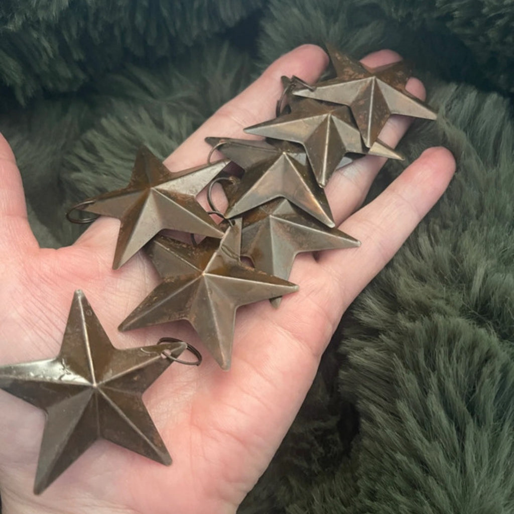Hand holding five metallic star-shaped objects against a green textured background