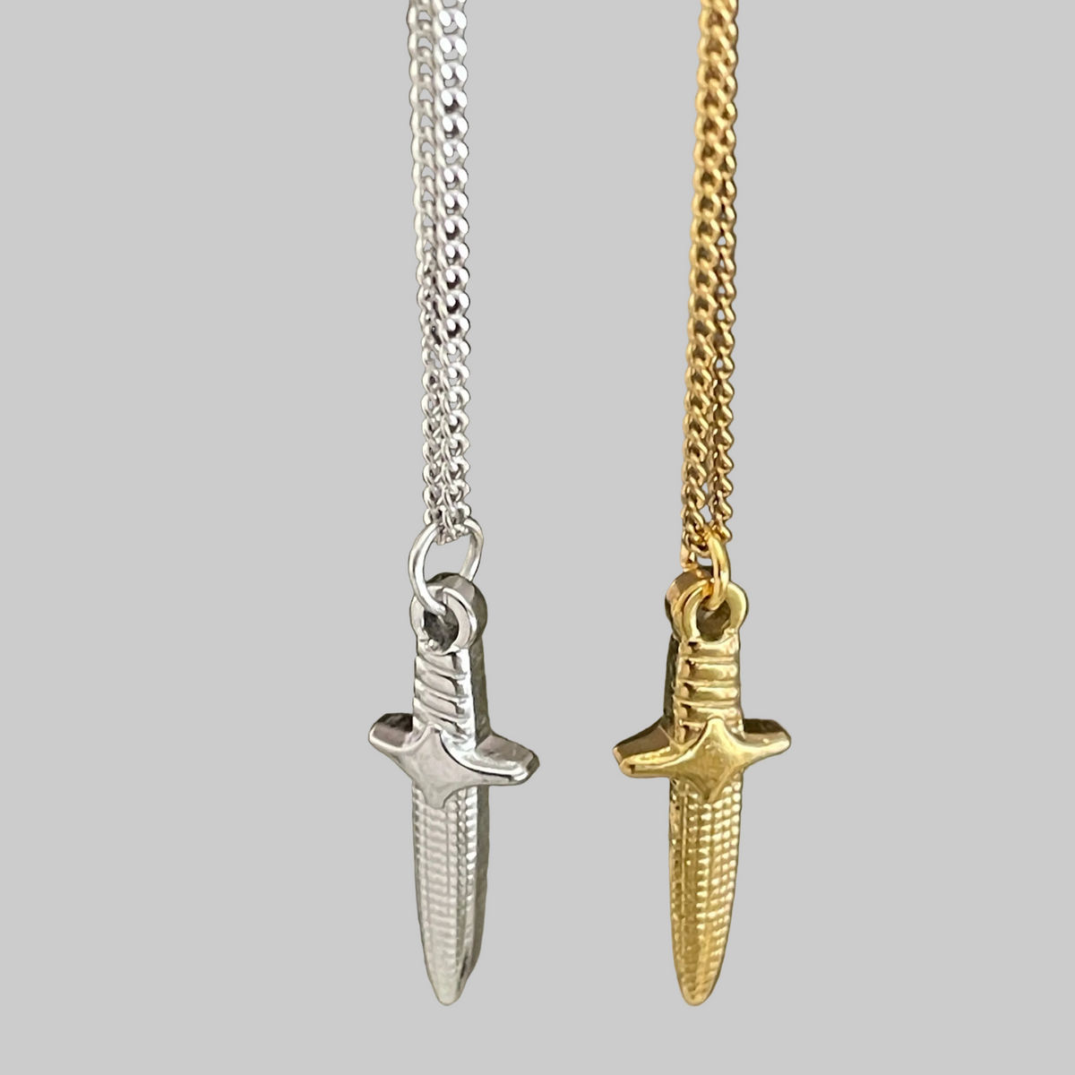 Two sword-shaped pendants on chains against a grey background