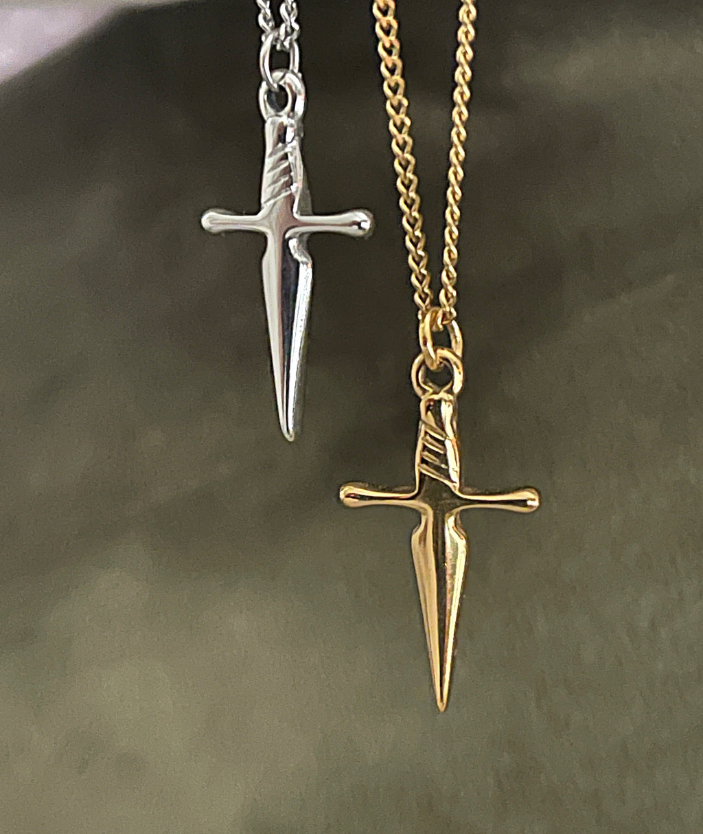 Gold and silver dagger-shaped pendants on chains against a dark background