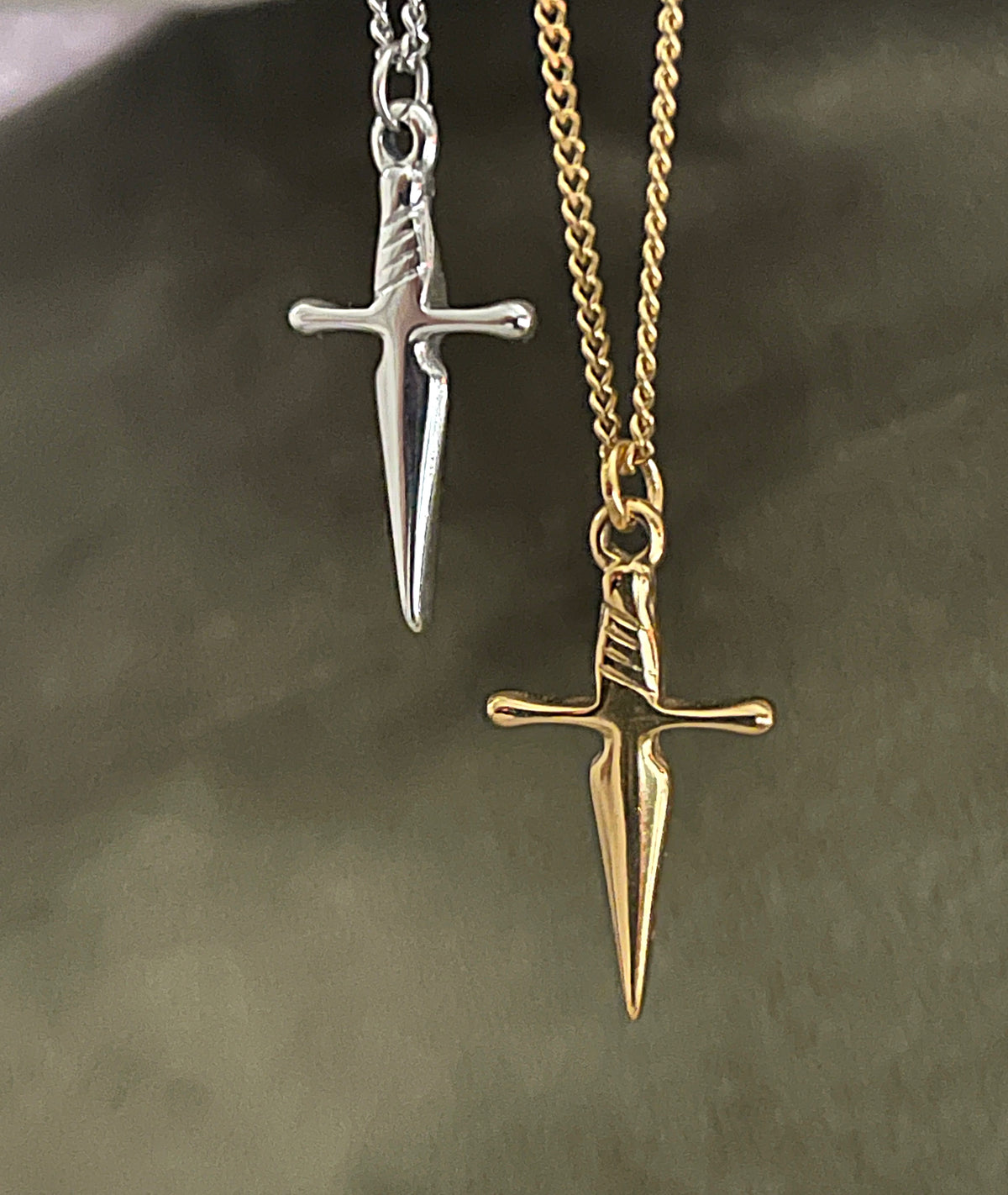 Gold and silver dagger-shaped pendants on chains against a dark background