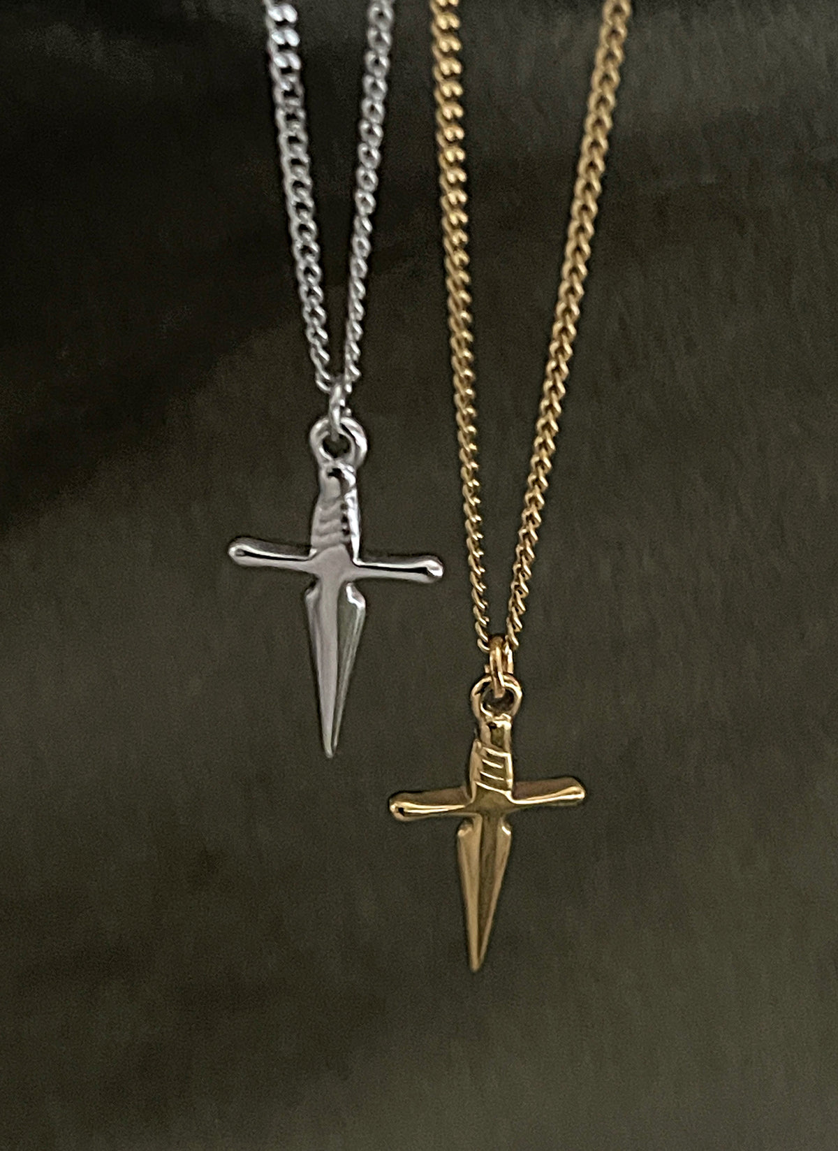 Two necklaces with sword pendants, one silver and one gold, on a dark background.