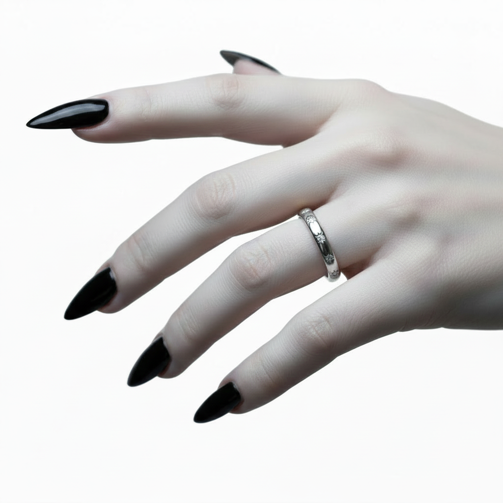 A close-up of a hand with long, glossy black stiletto-style nails wearing a simple silver band ring, set against a clean white background.