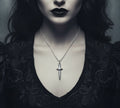 Person wearing a black lace garment with a silver dagger pendant necklace.