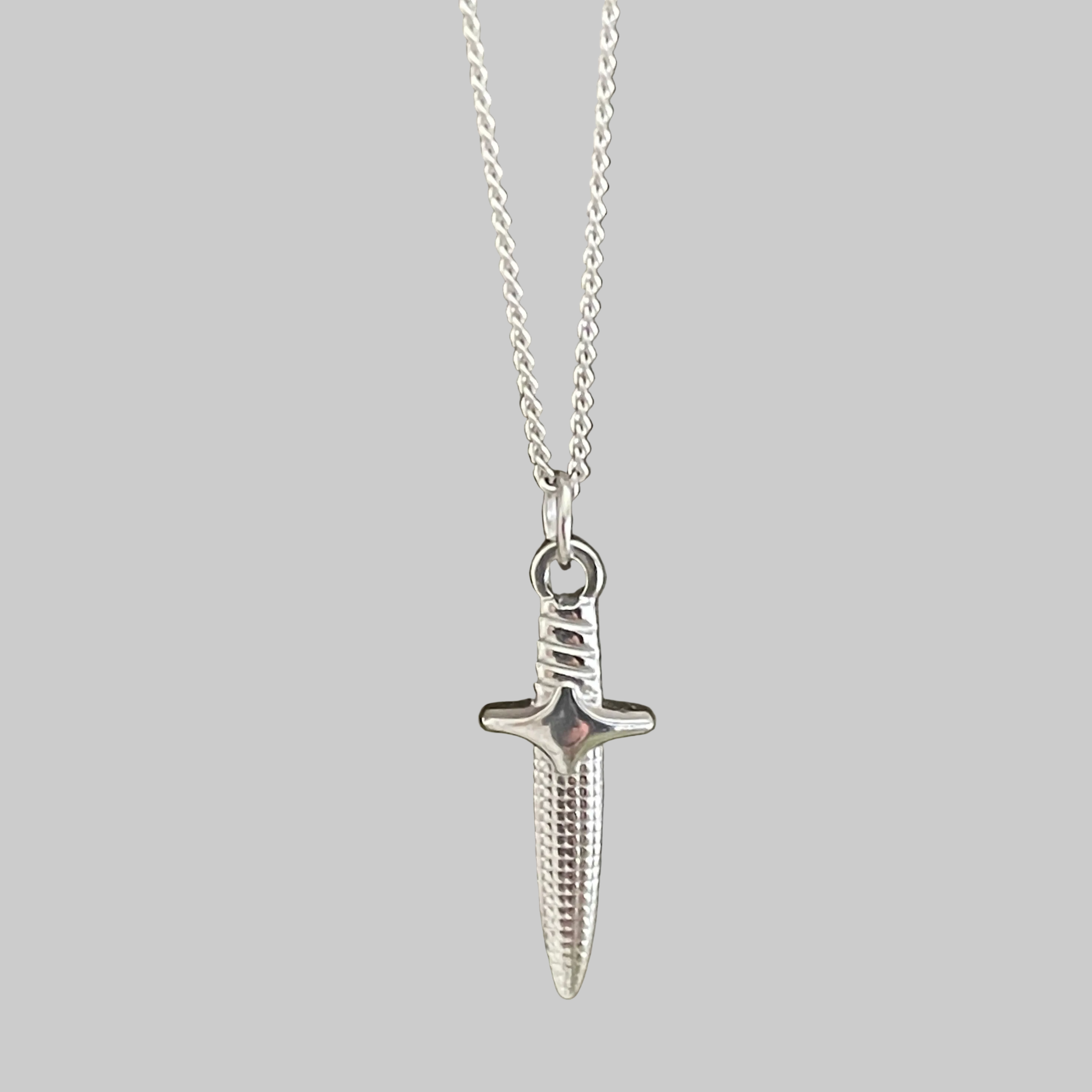 Silver dagger-shaped pendant on a chain against a grey background