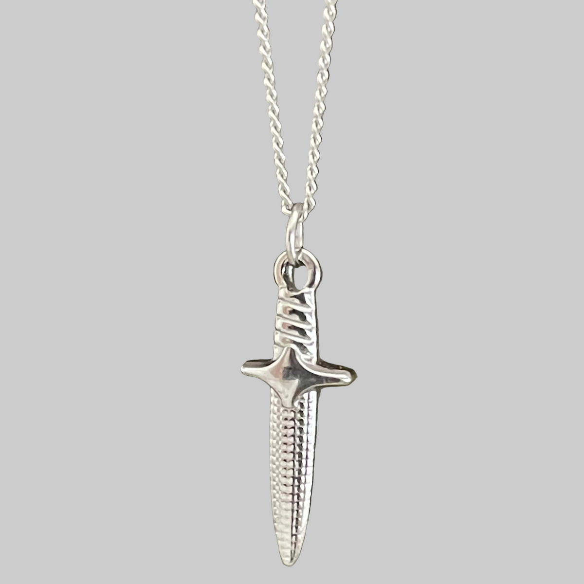 Silver dagger pendant on a chain against a grey background