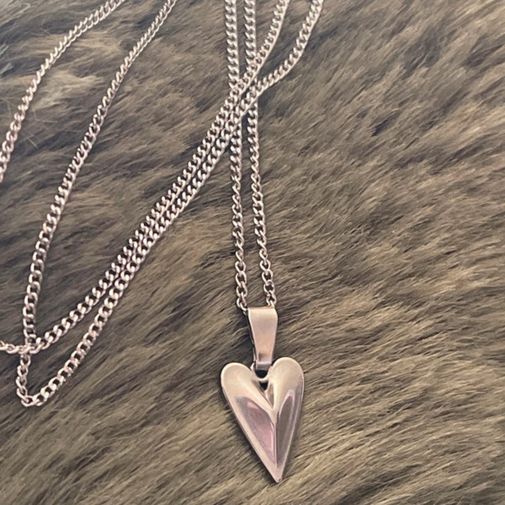 Heart-shaped silver pendant on a chain against a brown textured background