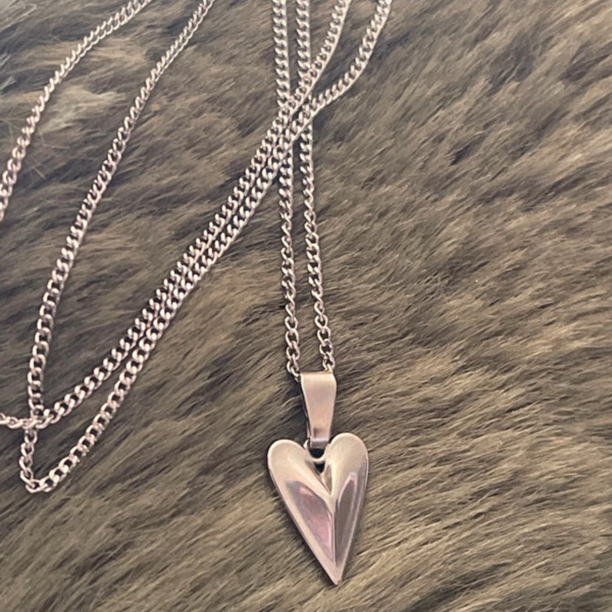Heart-shaped silver pendant on a chain against a brown textured background