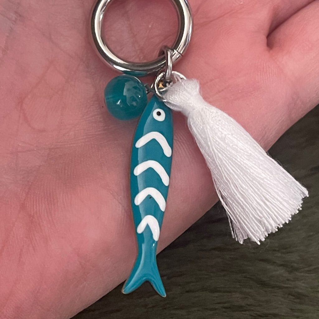 Turquoise fish-shaped necklace with white tassel held in a hand