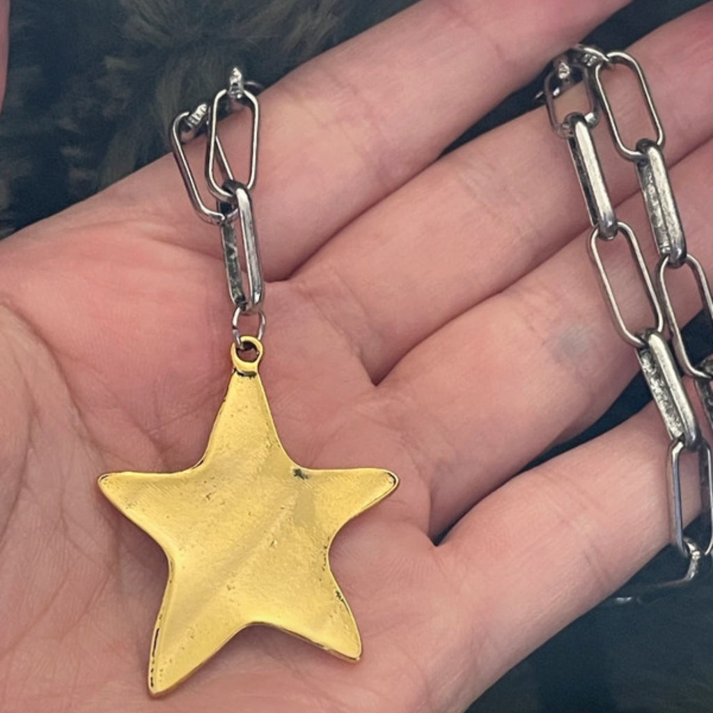 Gold star pendant on a chain held in a hand