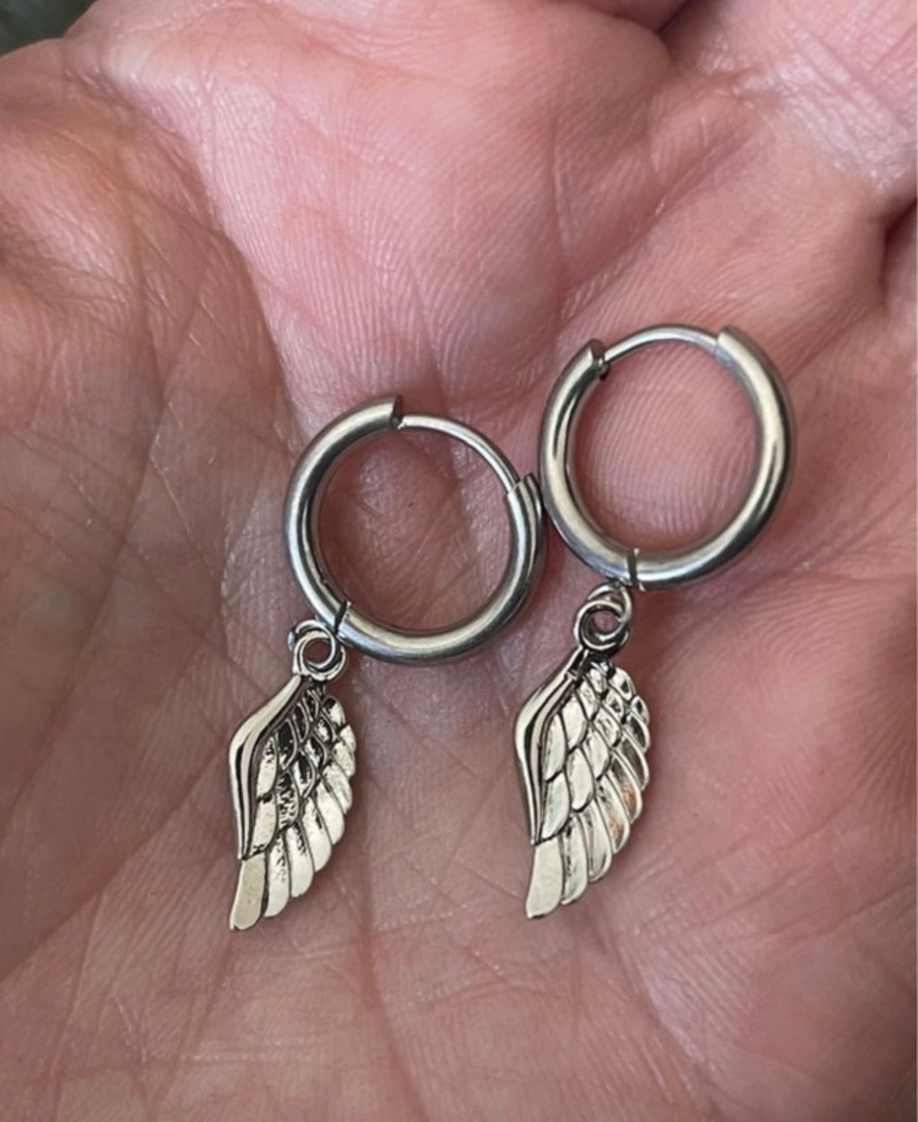 Silver hoop earrings with wing charms held in a hand.
