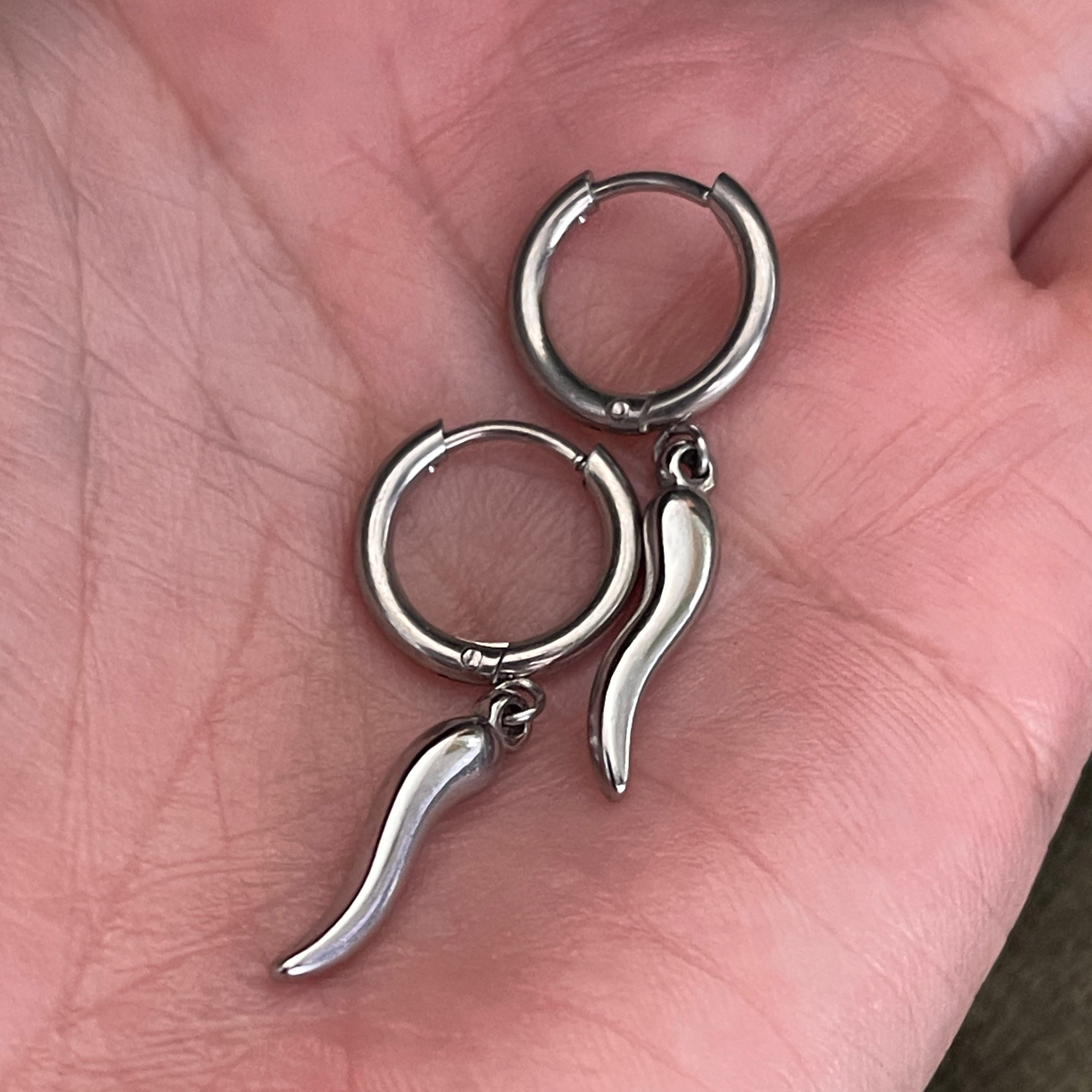 Silver hoop earrings with unique designs held in a hand.