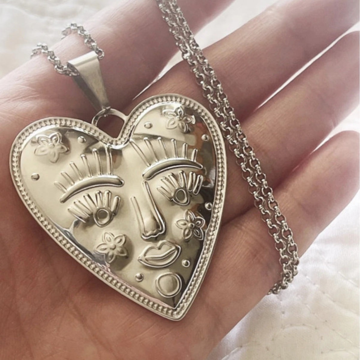 Silver heart-shaped pendant with face design held in a hand