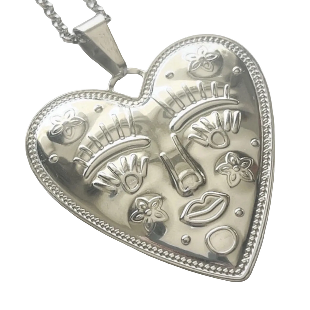Silver heart-shaped pendant with engraved designs on a white background