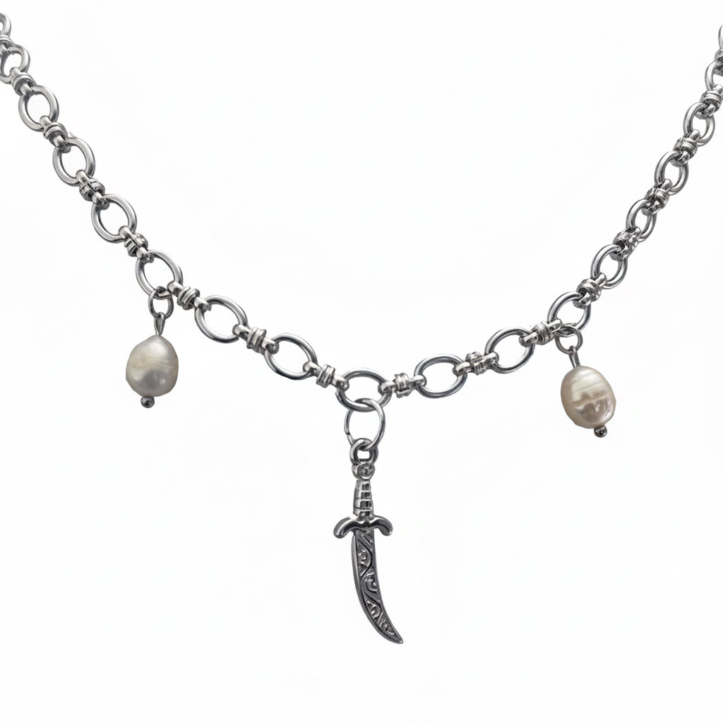 A silver-tone chain necklace featuring a central curved dagger pendant, flanked by two small, irregular white pearl beads on either side of the chain, shown against a plain white background.