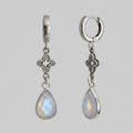A pair of silver dangle earrings with teardrop-shaped iridescent moonstone drops and ornate filigree details, shown against a solid grey background.