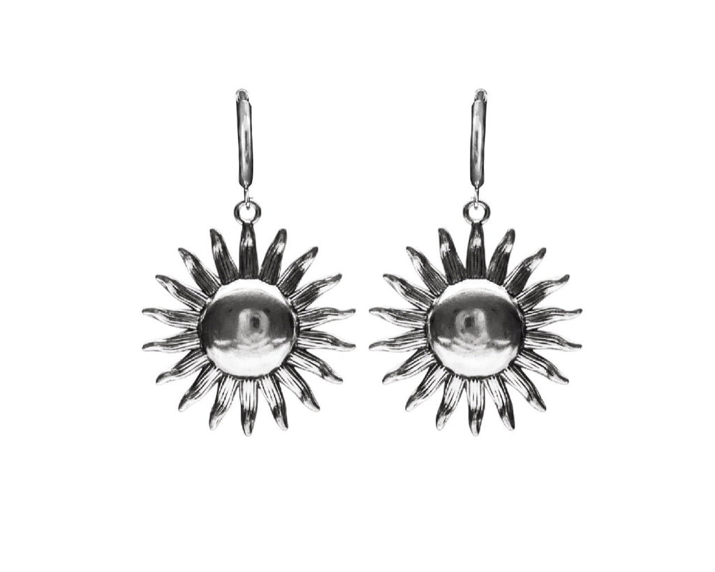 A pair of silver sunburst drop earrings with a polished central circle and textured radiating points, shown against a plain white background.