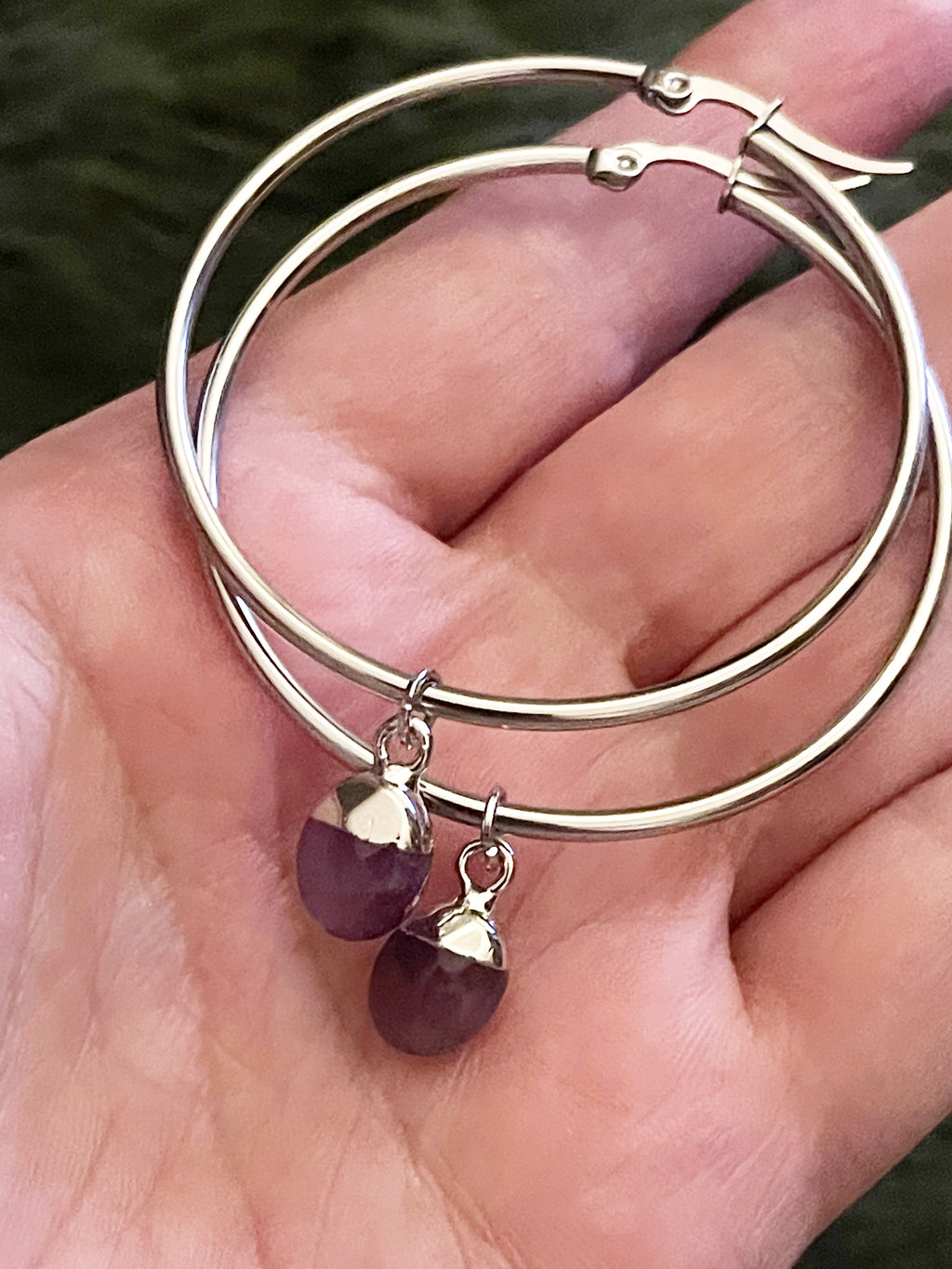 Silver hoop earrings with purple  crystal on a hand